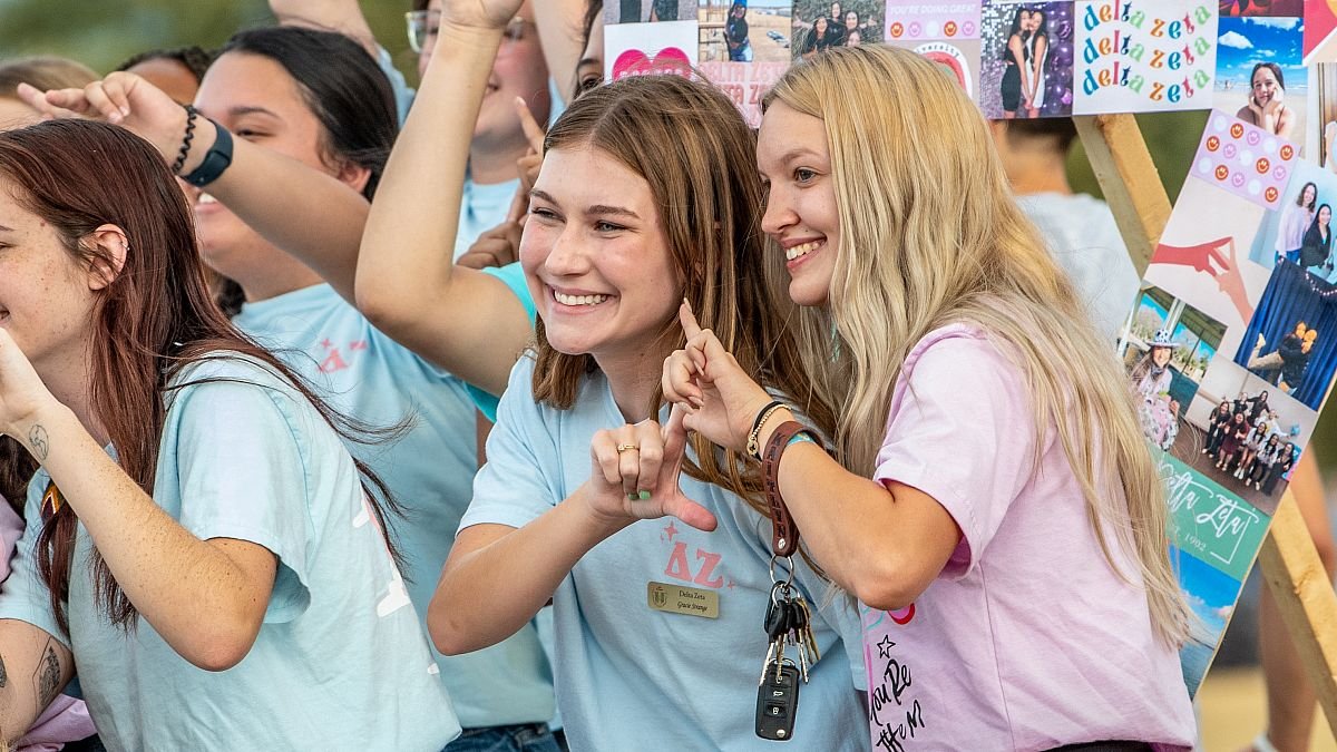 Sorority women smiling and giving their hand sign at a Greek life event